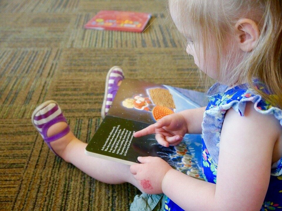 una bambina seduta sul pavimento a leggere un libro