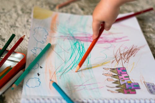 a child is drawing with colored pencils on a piece of paper
